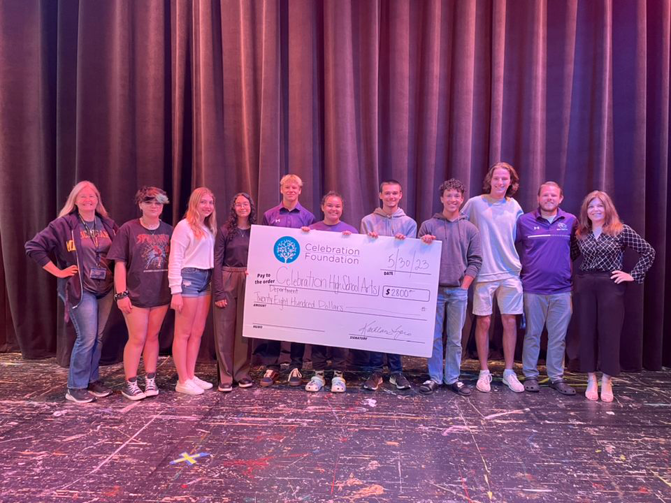 Children standing on stage holding a large, fake check for $1,400